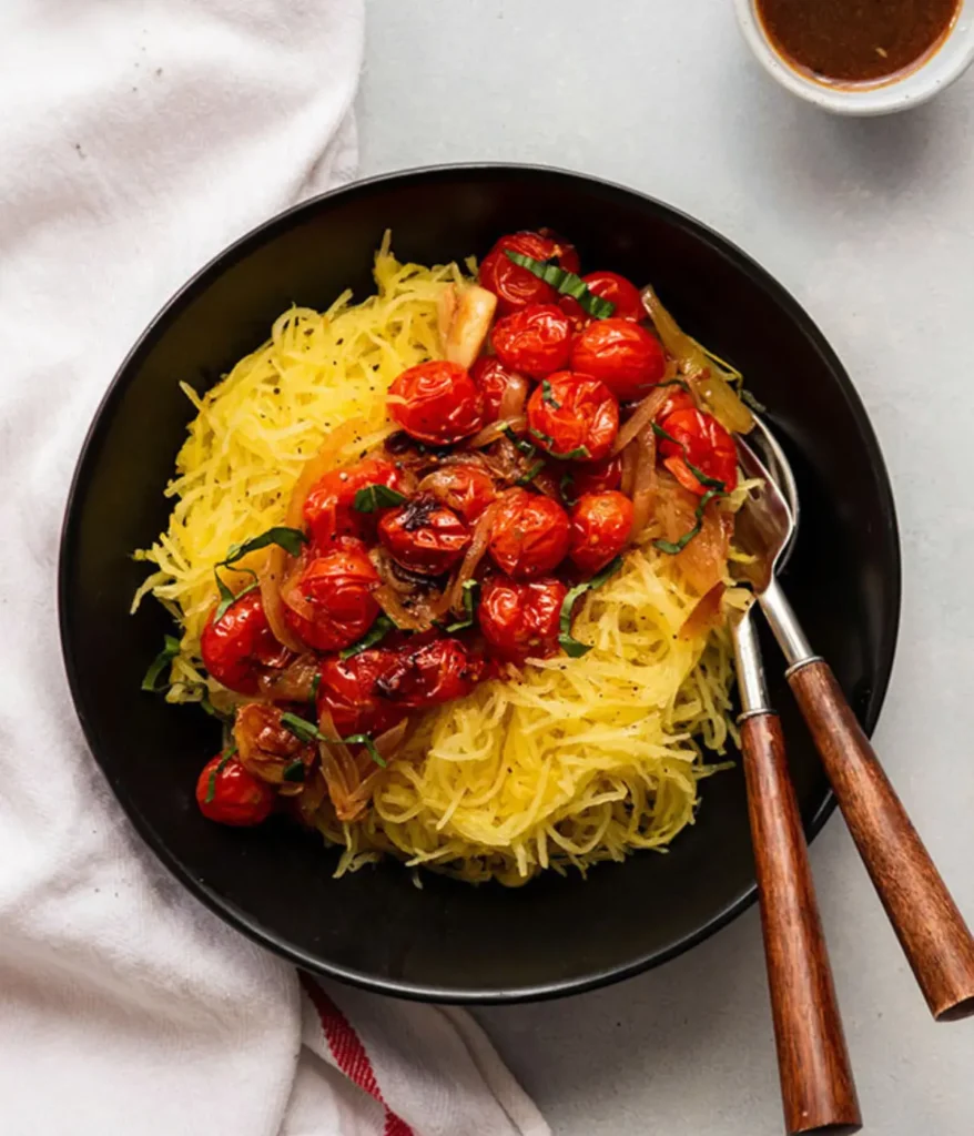 A bowl of spaghetti squash topped with roasted tomatoes on a table.