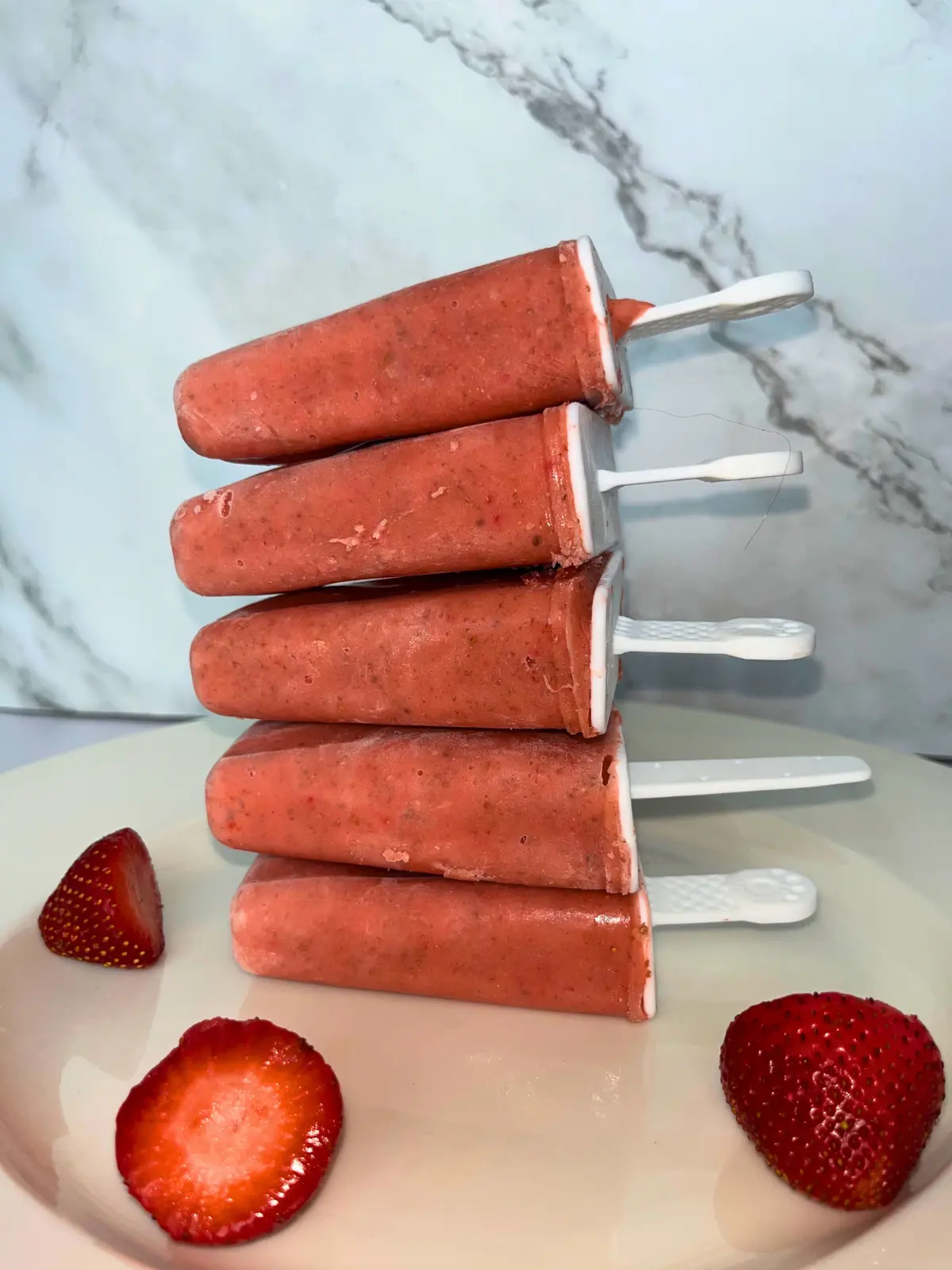 Strawberry mango popsicles with immune boosting nutrients stacked on top of one another on a plate.