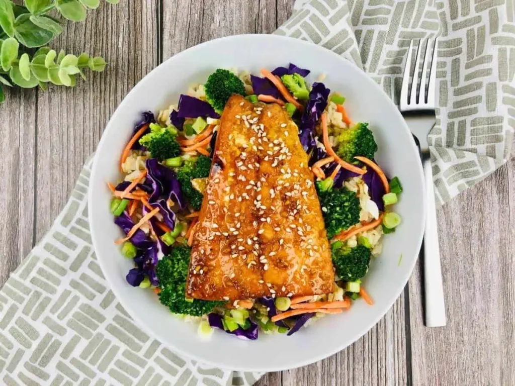 A gluten-free teriyaki salmon bowl on a table next to a fork.