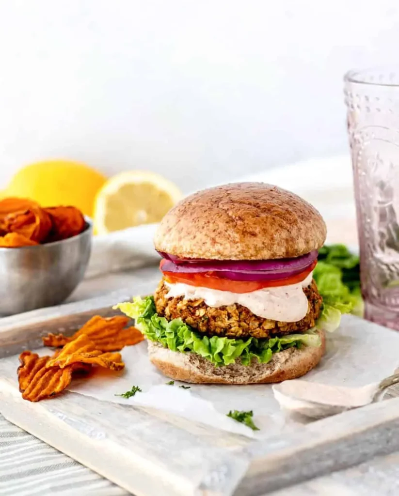 A chickpea burger with oats fully assembled on a plate on a dining table.