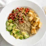 A birds-eye view of a tofu edamame bowl on a table next to a napkin and fork.