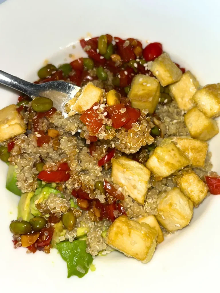 A close-up of the tofu, edamame, quinoa and veggie bowl mixed together with the sauce with a forkful in the forefront.