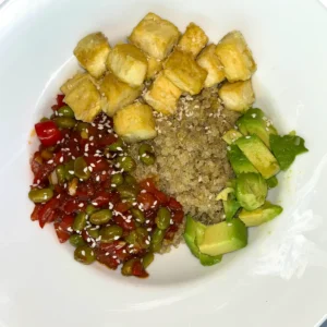 A close-up of a tofu, edamame, and quinoa bowl with a stir-fry sauce and veggies.