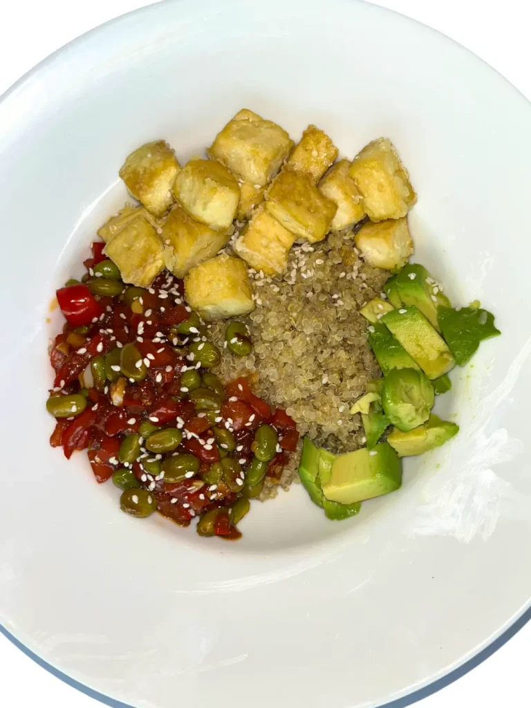 A close-up of a tofu, edamame, and quinoa bowl with a stir-fry sauce and veggies.