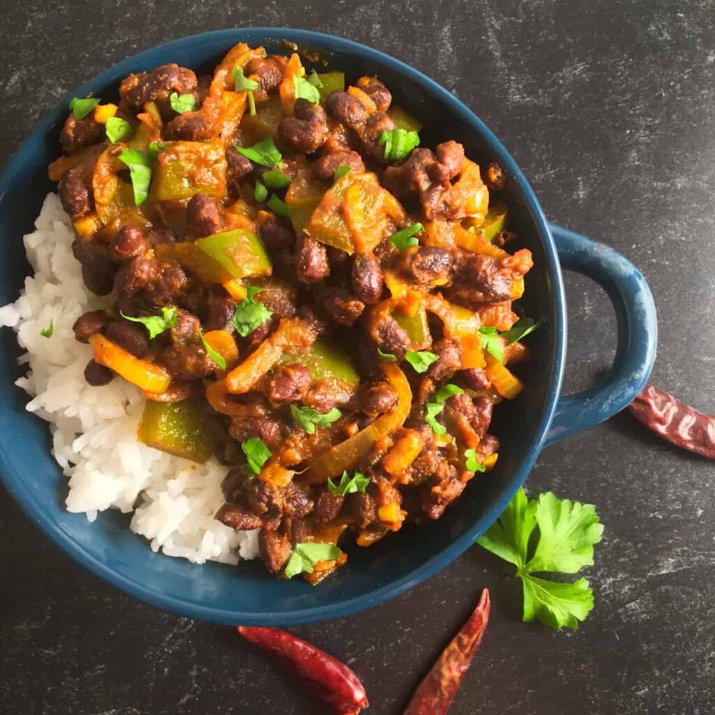 A bowl of black bean curry with rice on a table.