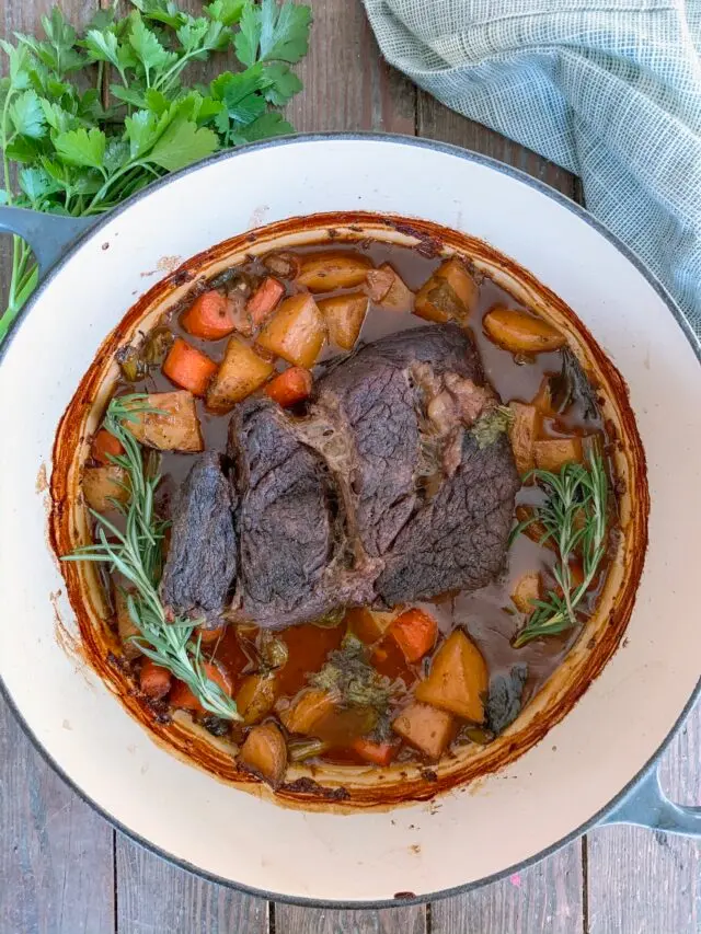 A pot roast with carrots and potatoes in a Dutch oven.