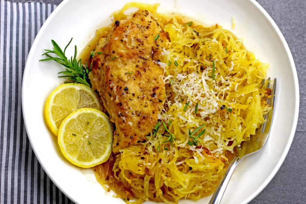 Braised chicken with spaghetti squash and lemon slices in a white bowl.