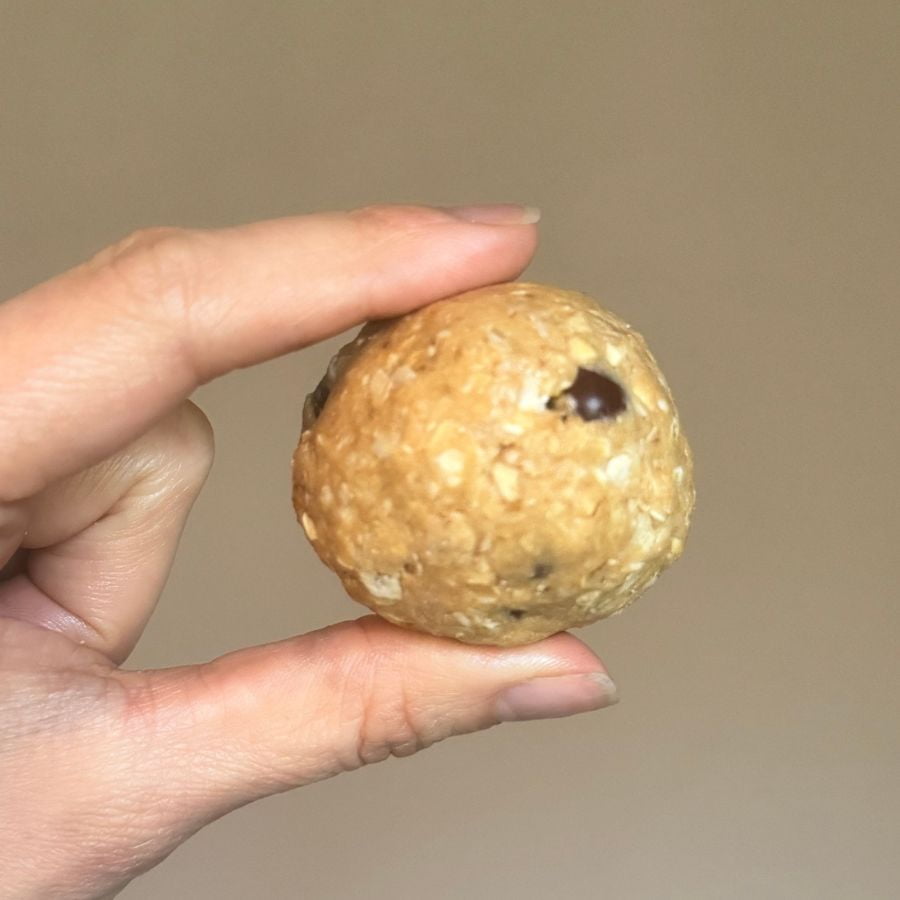 An oatmeal protein ball in between someone's pointer and thumb fingers.