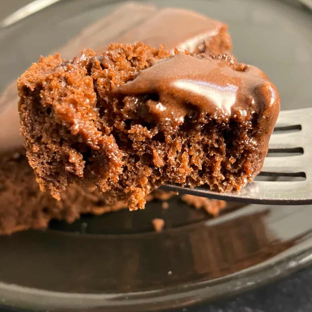 A slice of chocolate cake with protein powder topped with chocolate frosting on a plate.