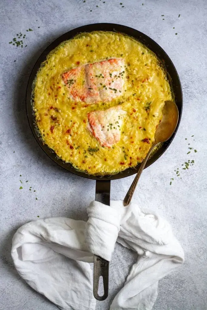 Salmon filets and spaghetti squash with a creamy sauce in a cast iron skillet on a table.