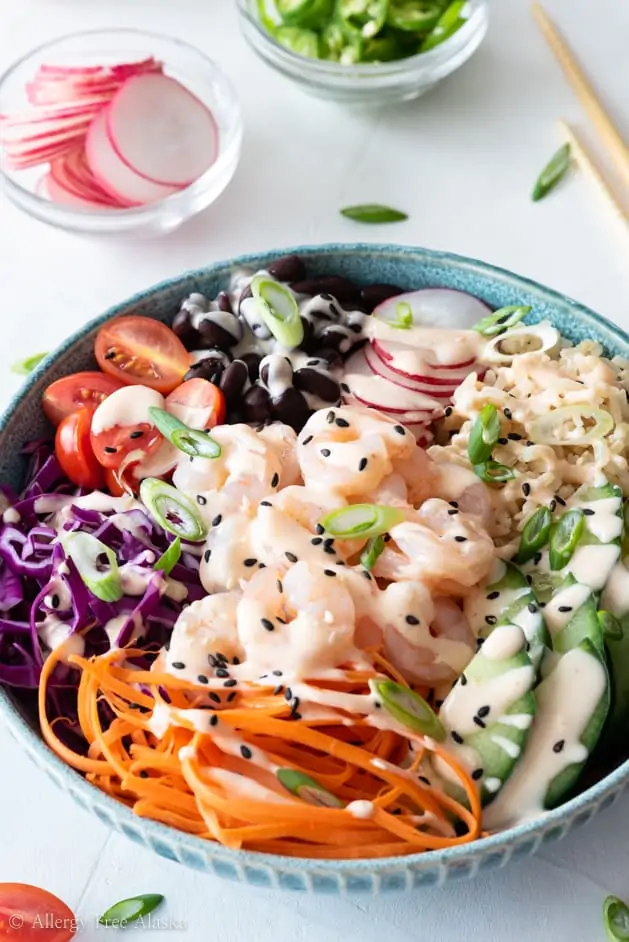 A shrimp poke bowl drizzled with spicy sriracha sauce on a table next to chopsticks.