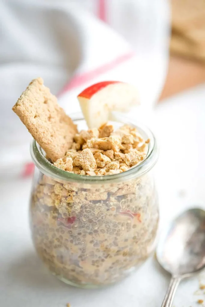 Apple and chia pudding overnight oats in a glass, topped with a graham cracker and apple slice.