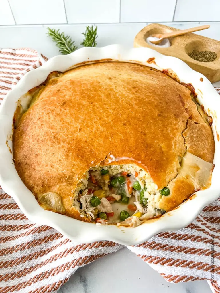 Bisquick chicken pot pie in a casserole dish after baking on a red and white striped towel on the counter.