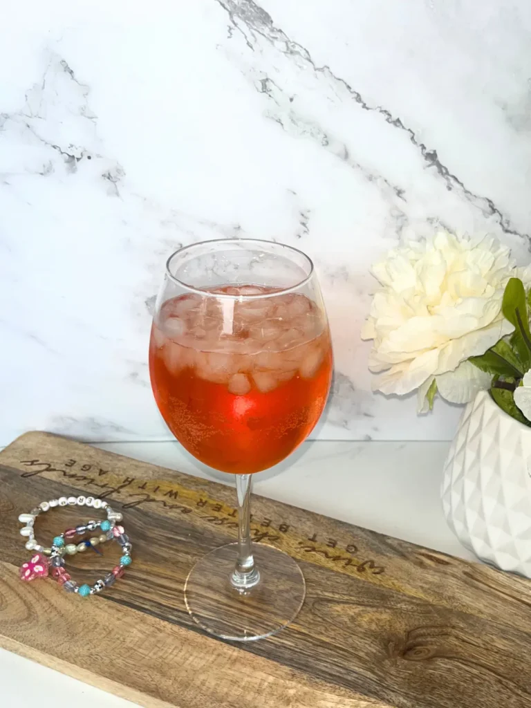 A glass of champagne spritz on a wood cutting board next to friendship bracelets.