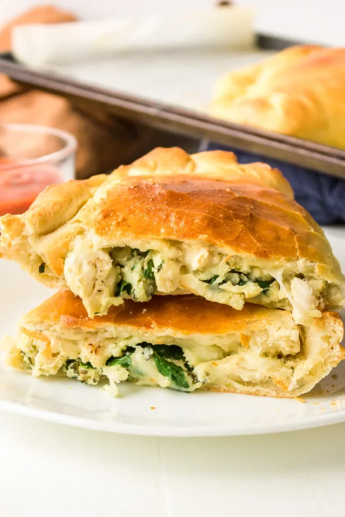 A creamy chicken calzone cut in half and stacked on top of one another on a white plate.