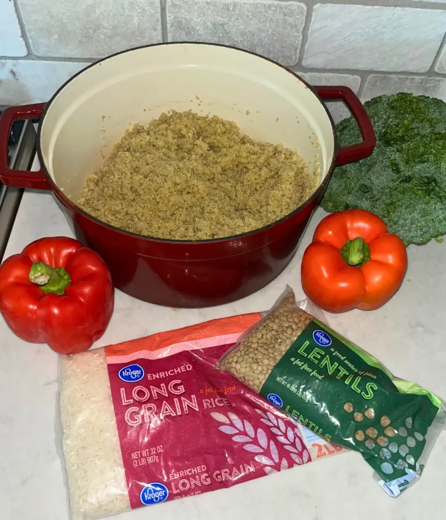 A large pot of quinoa on a counter next to a bag of uncooked rice and a bag of uncooked lentils.