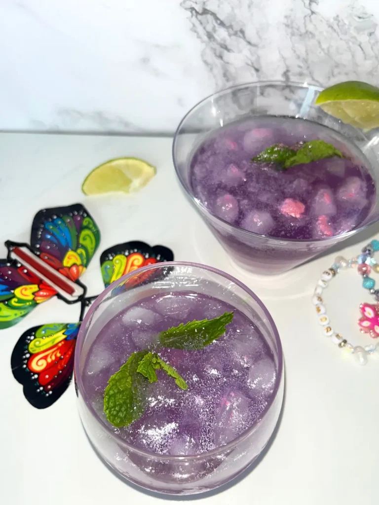 Two purple Empress gin cocktails in glasses garnished with lime on a counter next to friendship bracelets.