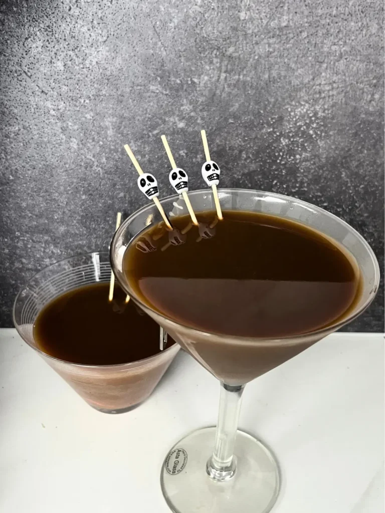 Two chocolate espresso martinis on a counter, garnished with skull toothpicks.