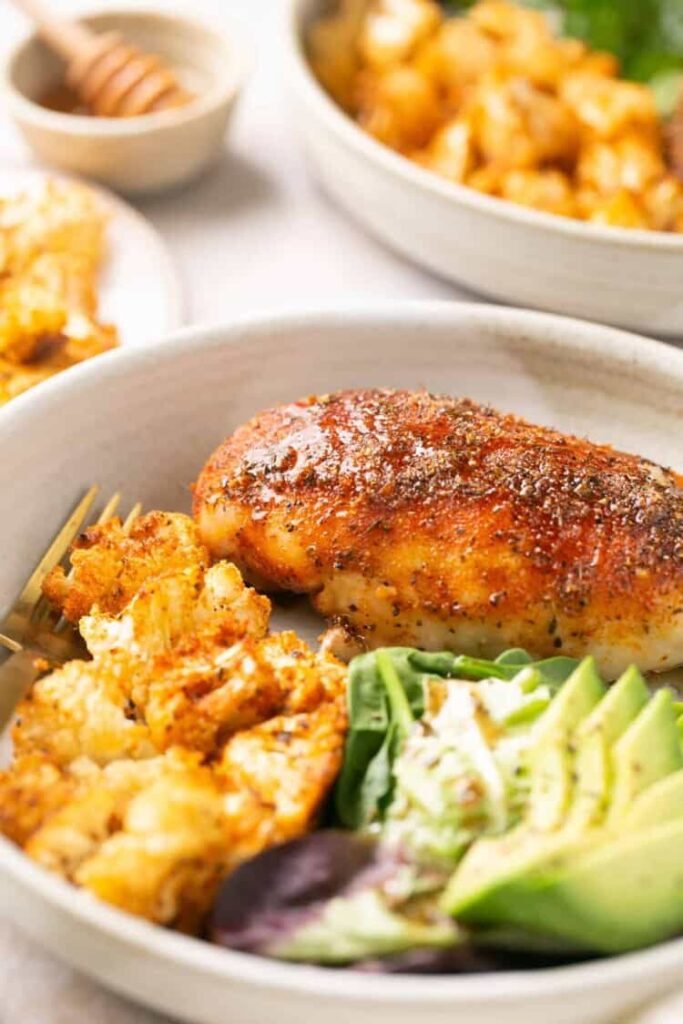 Honey garlic chicken breast, roasted cauliflower and avocado slices on a plate on a table.