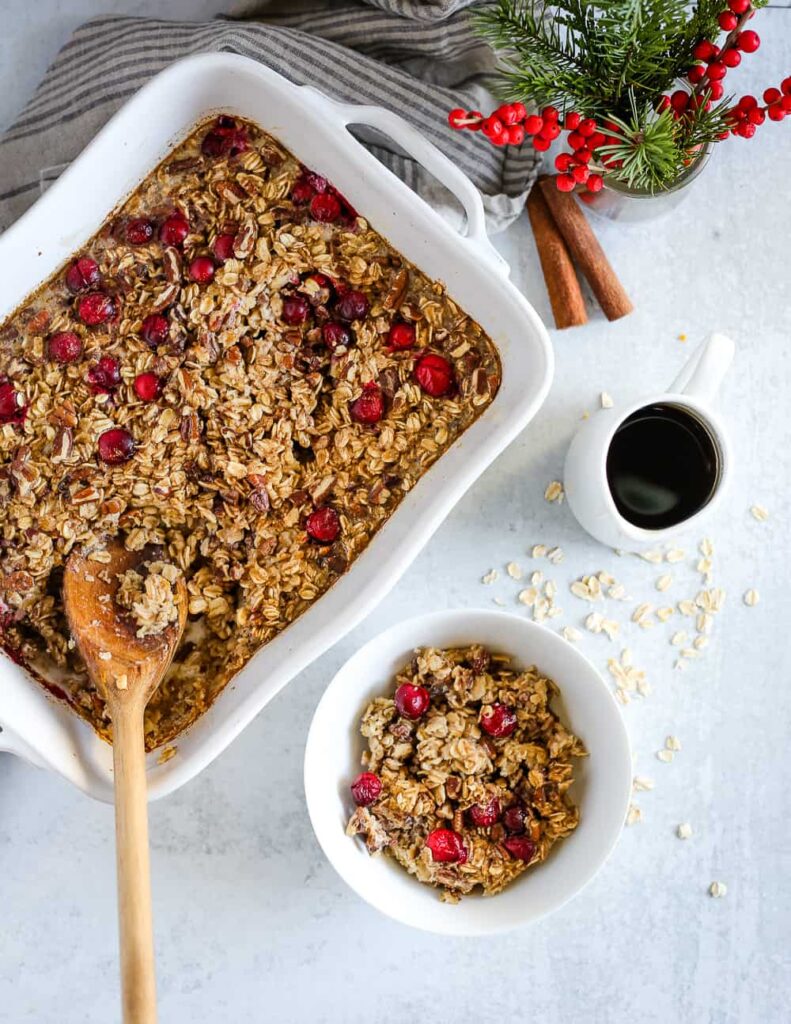 A large pan of maple pecan cranberry baked oatmeal with a wooden spoon in it on a table.