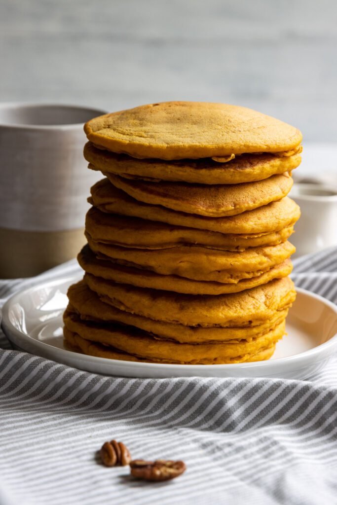 A large stack of pumpkin pancakes on a white plate on a table.