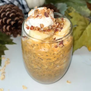 A glass jar of pumpkin cheesecake protein overnight oats on a counter with pumpkin wreath behind it.