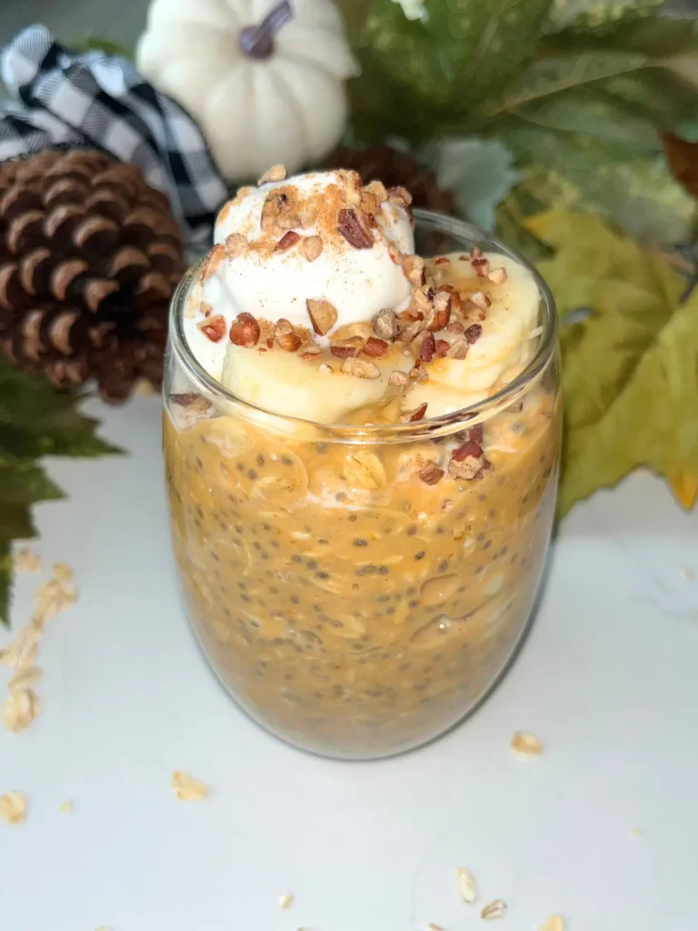 A glass jar of pumpkin cheesecake protein overnight oats on a counter with pumpkin wreath behind it.