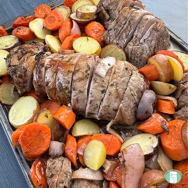 A baked pork tenderloin with roasted carrots and potatoes on a sheet pan.