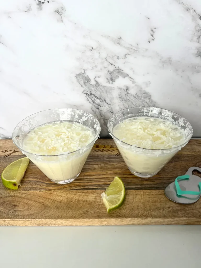 Two coconut snow on the beach cocktails on a wood cutting board garnished with lime.