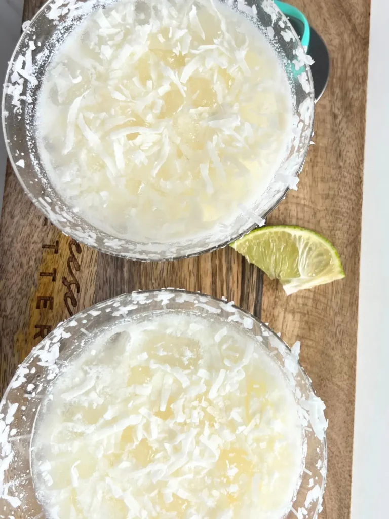 A close-up birds-eye view of two snow on the beach cocktails with shredded coconut on top.