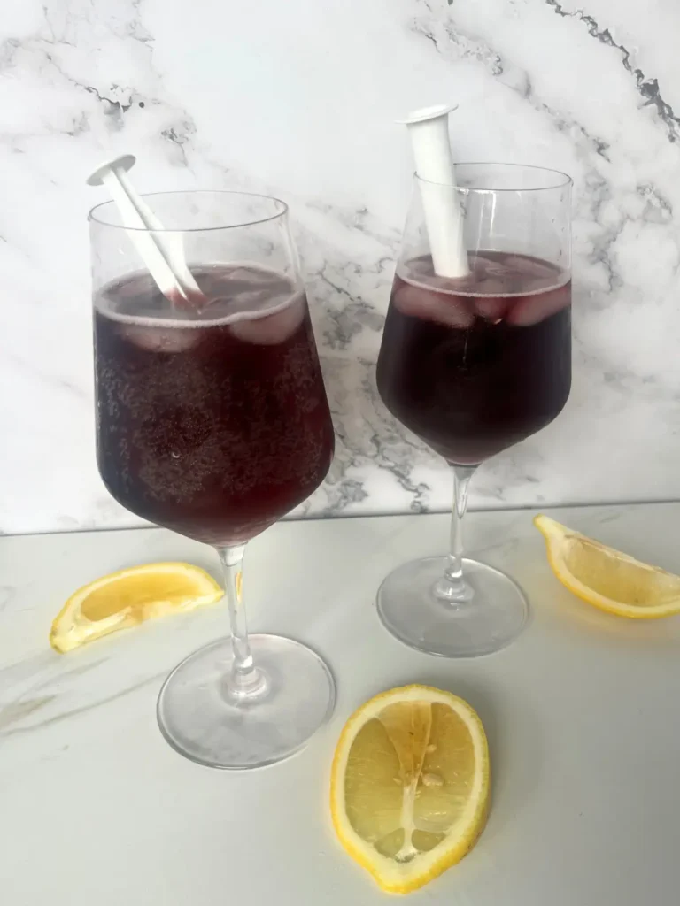 Two red wine spritzers in wine glasses with syringes inside.