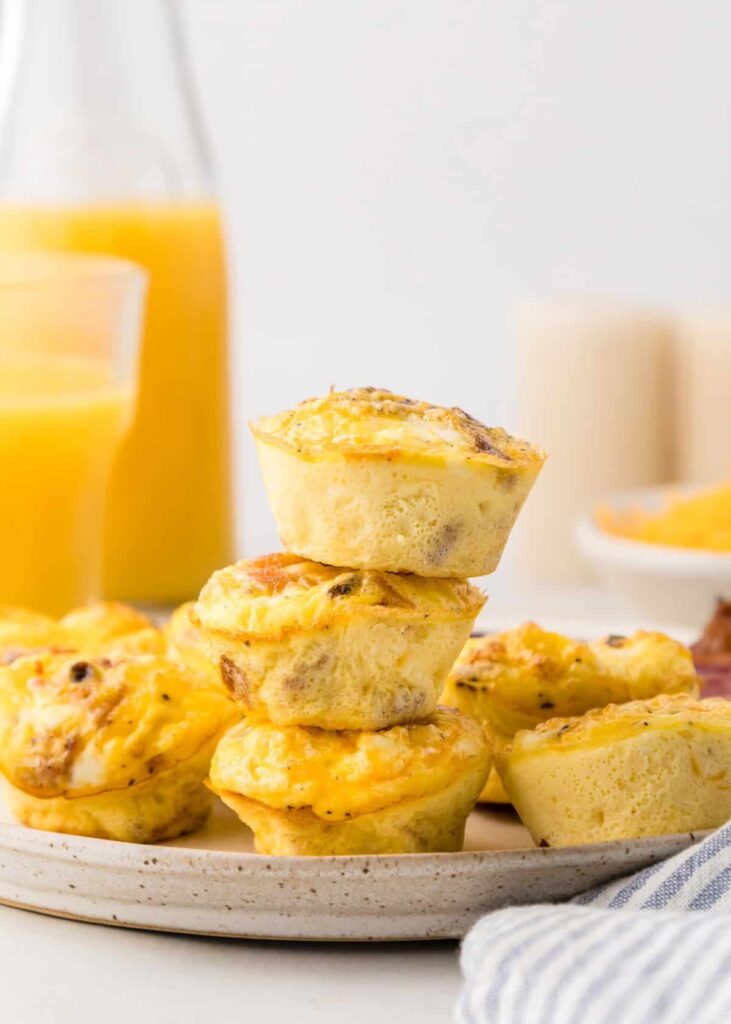 Bacon and egg muffin bites stacked on a plate next to a glass jar of orange juice.