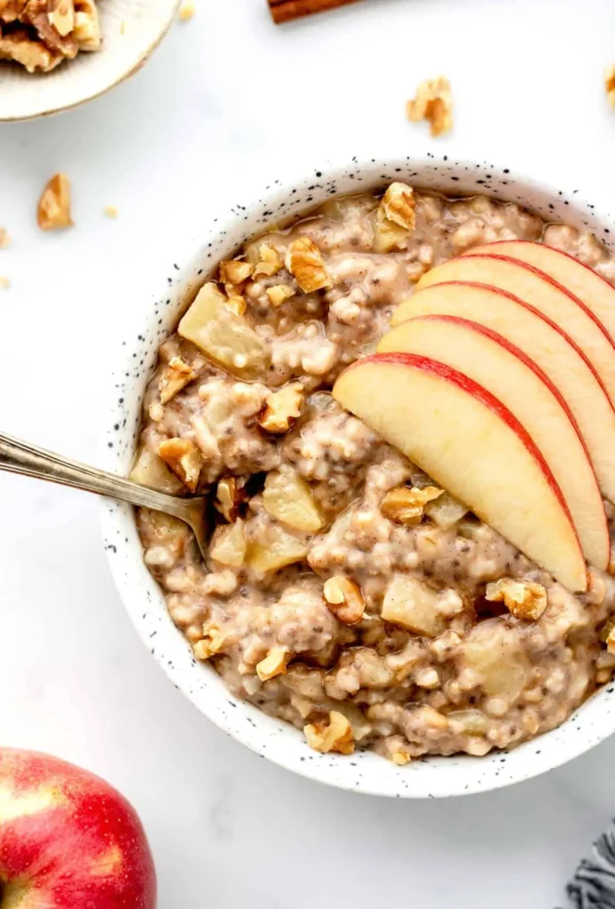 A close-up of a bowl of crockpot cinnamon oatmeal with apple slices on top.