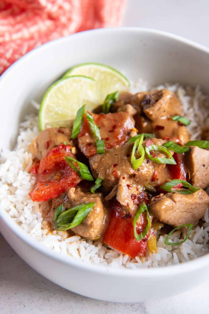 Slow cooker Asian pork with bell peppers served over rice in a white bowl on the table.