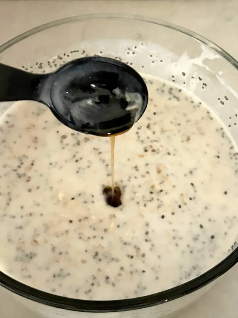 Pouring maple syrup into the overnight oats mixture before refrigeration.