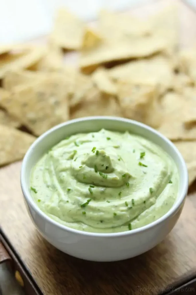 A bowl of avocado ranch dip with Greek yogurt next to chips on a cutting board.