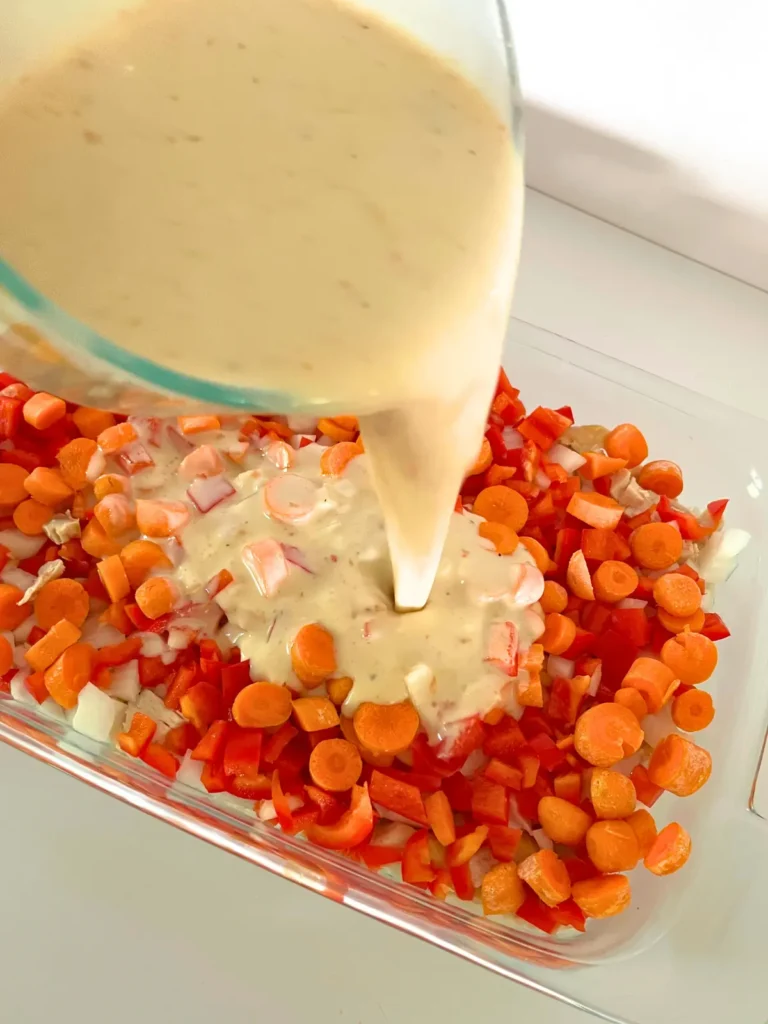 Pouring the creamy coconut milk mixture over the raw veggies and chicken in a casserole dish.