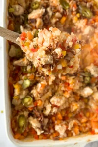 A big wooden spoonful of the coconut chicken and chopped pecan casserole over a casserole dish.