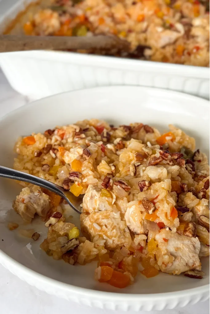 A plate of the creamy coconut chicken and rice casserole with a fork digging into it with a casserole in the background.