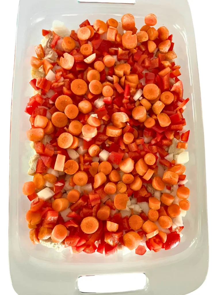 A baking dish with diced carrots, diced bell peppers, rice and chicken.