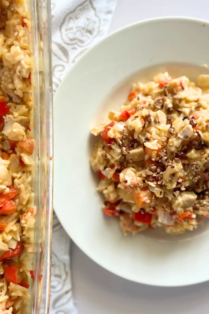 A plate of coconut rice, chicken and carrots next to the casserole dish on a counter.