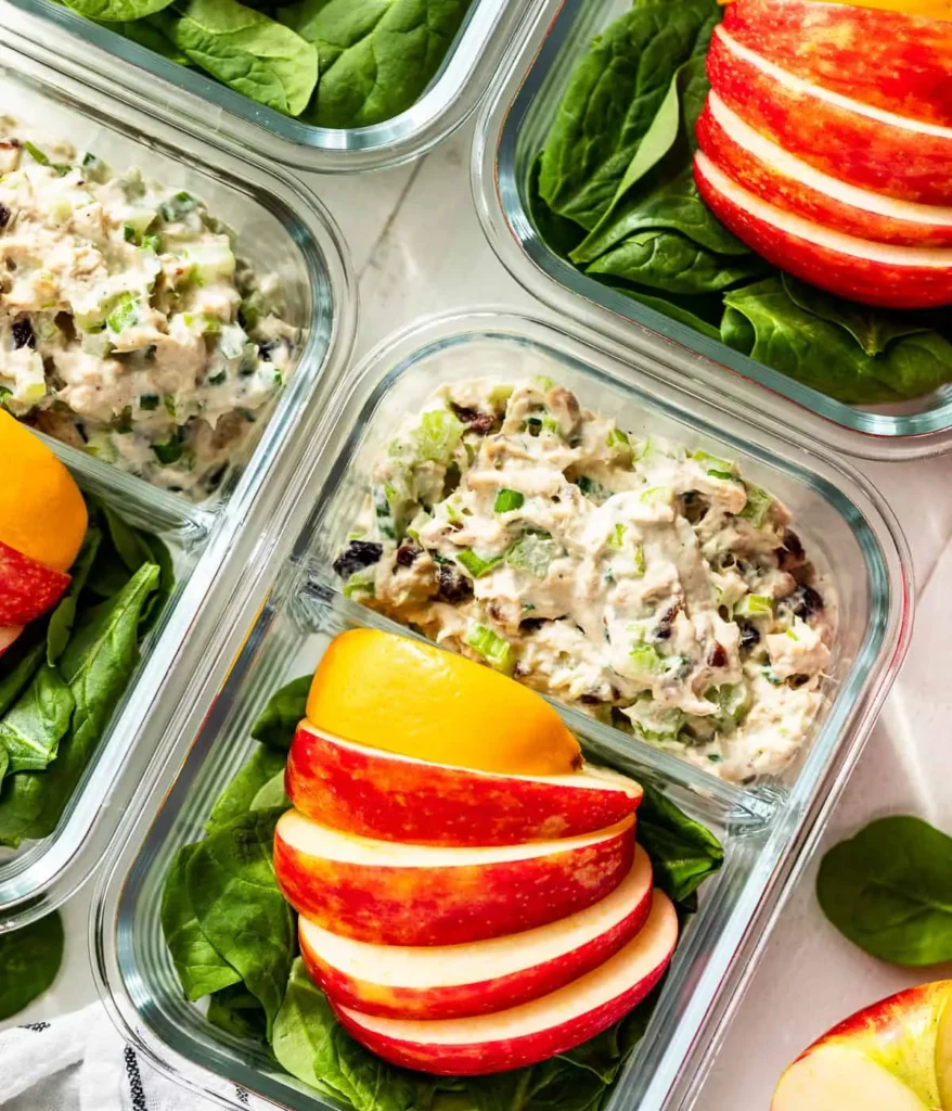 Tuna salad in a lunch box next to a salad topped with apples.