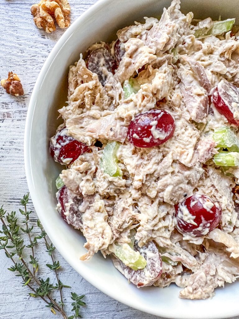 A bowl of hearty California chicken salad with grapes on a table.