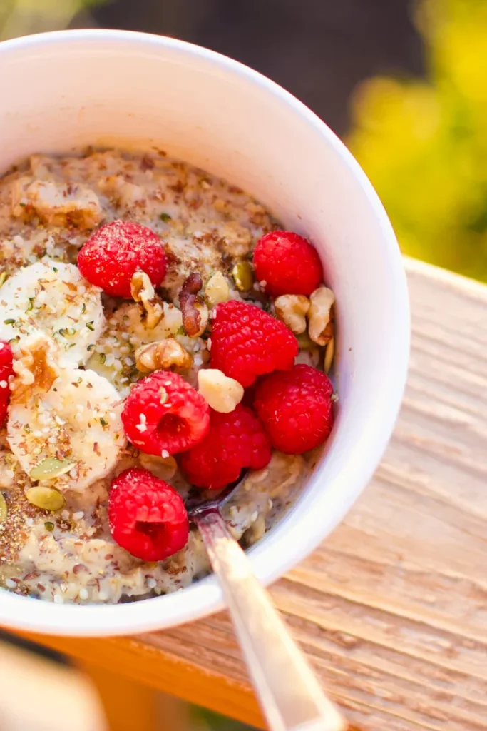 A bowl of high protein vegan oatmeal topped with raspberries and bananas on a counter.