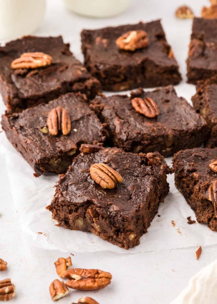 Sliced sweet potato brownies on parchment paper topped with a pecan on each one of them.