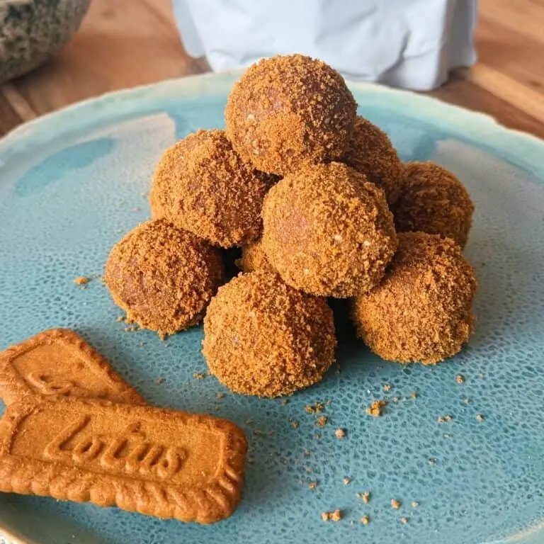 Biscoff protein balls stacked on top of one another on a blue plate next to two Biscoff cookies.