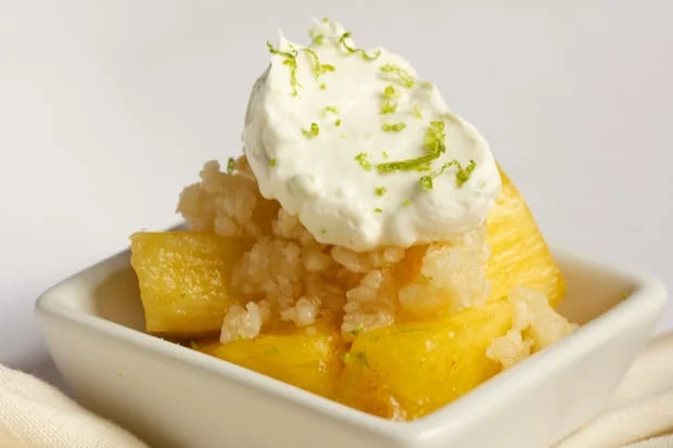 A bowl of pineapple topped with coconut lime whipped cream and a macadamia topping. 