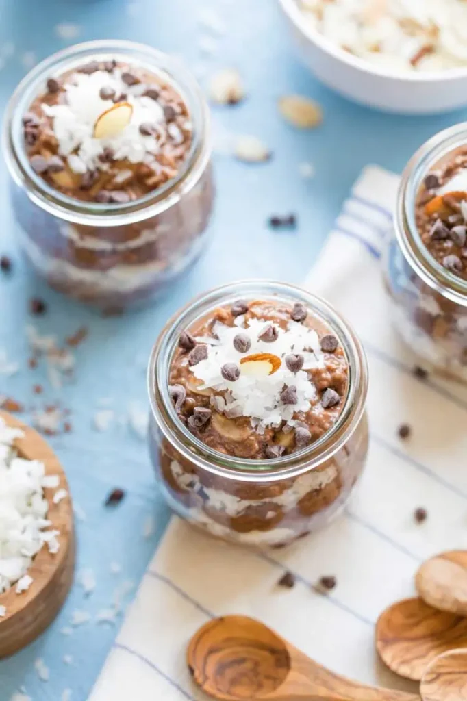 Two glass jars of chia seed pudding topped with chocolate chips and coconut flakes on a counter.