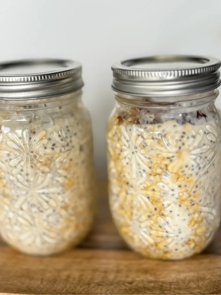 Two mason jars of maple brown sugar overnight oats with lids on them on a wood cutting board.