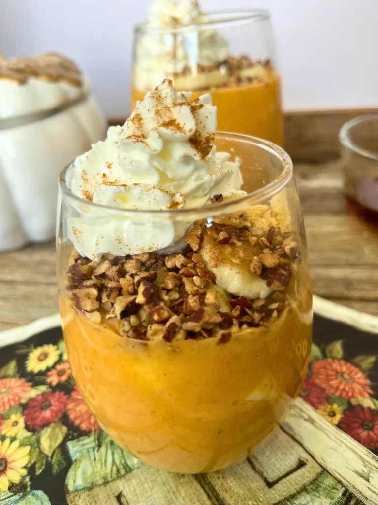 A close-up of the healthy pumpkin cheesecake pudding in a glass cup topped with banana slices, pecans and whipped cream.